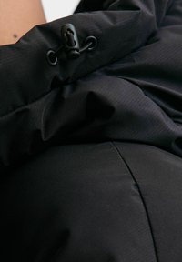 Tessuto di giacca a vento nera con una texture increspata. Presenta una chiusura a strappo e dettagli di cucitura. Finitura opaca con un design elegante.