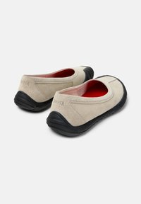 Chaussures en daim beige au design arrondi, semelles en caoutchouc noir et semelles intérieures rouges ; avec logo embossé à l'arrière.