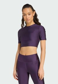 Top atlético corto morado hecho de material brillante y elástico, combinado con leggings de talle alto a juego que presentan una marca minimalista.