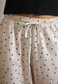 White pajama pants with black polka dots and an elastic waistband tied with a white drawstring, worn with a black top.