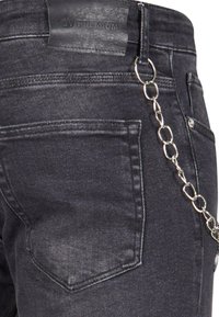 Mustat farkut, joissa on teksturoitu nahkaliLabels, kaksi takataskua ja hopeaketju kiinnitettynä vyölenkkiin.