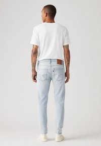 Τζιν παντελόνια ανοιχτού τόνου με καφέ δερμάτινο έμπλαστρο στο πίσω μέρος και πίσω τσέπες, συνδυασμένα με ένα απλό λευκό t-shirt και μπεζ παπούτσια.