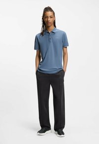 Hellblaues Poloshirt mit einer Knopfleiste mit drei Knöpfen, versehen mit einem kleinen Logo. Kombiniert mit dunkelgrauen, weit geschnittenen Hosen und schwarzen Sneakern.