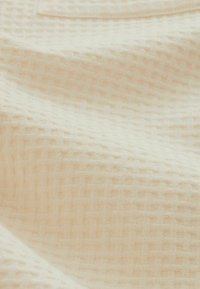 Tissu beige doux avec une texture gaufrée subtile et des plis doux créant un motif ondulé sur la surface.