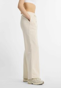 Pantalon de survêtement couleur crème avec taille à cordon, poches latérales et coupe droite. Tissu doux avec une texture lisse.