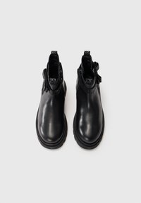Botas de cuero negro hasta el tobillo con un acabado suave, paneles laterales elásticos texturizados y una suela resistente. Punta redondeada y tirador en la parte trasera.
