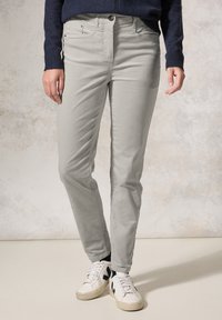 Pantaloni in twill di cotone grigio chiaro con una vestibilità slim, cinque tasche e chiusura con bottone, abbinati a sneakers bianche con accenti neri.