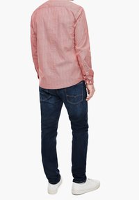 Camisa de manga larga de rayas rojas con cuello abotonado, combinada con jeans de mezclilla azul oscuro y zapatillas blancas.