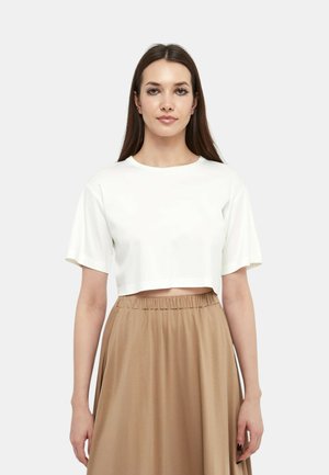 Maglietta bianca corta con maniche corte, abbinata a una gonna beige fluida con vita elasticizzata. Tessuto morbido e design semplice.