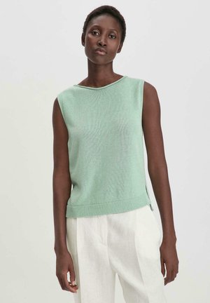 Mintgroene mouwloze trui met een ronde hals, geribbelde textuur en zijsplitten. Gecombineerd met lichtgekleurde, losse broek.
