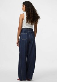 Bredde ben, mørke denimjeans med høy midje, synlige søm-detaljer, to baklommer og en jevn tekstur.