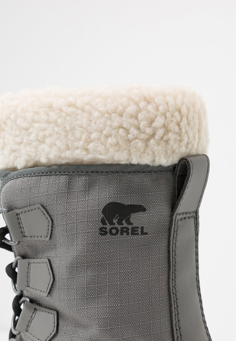 Grauer wasserdichter Stiefel mit einem flauschigen weißen Fleece-Kragen, strukturiertem Obermaterial, schwarzem Logo und Schnürdesign für einen sicheren Sitz.