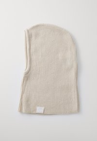 Knit beanie in light beige, featuring a ribbed texture. Includes a small, white logo patch at the hem. Form-fitting design with a tapered top.