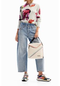 Světlý šedý svetr s květinovými potisky, světlé modré volné džíny a vícebarevné tenisky. Drží krémovou tašku se šikmými pruhy a logem.