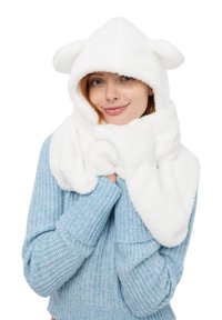 Biała polarowa chusta z kapturem i uszami misia, o miękkiej fakturze, owinięta wokół szyi, w połączeniu z jasnoniebieskim swetrem z prążkowanej dzianiny.