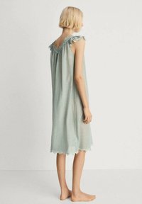 Vestito da notte verde senza maniche con scollatura rifinita in pizzo e dettagli di spalle a volant. Vestibilità fluida e leggermente ampia, che termina appena sopra le ginocchia.