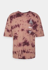 Hnědý tričko s tie-dye efekt, krátké rukávy, kulatý výstřih a grafické detaily v bílé barvě, včetně geometrických tvarů a textu.
