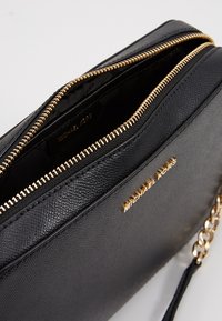 Borsa a tracolla in pelle nera con finitura testurizzata, con cerniera dorata e logo impresso sulla parte esterna. Include un dettaglio con tracolla a catena.