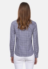 Camicia a quadretti navy e bianca con maniche lunghe, vestibilità slim, polsini con bottoni e orlo curvo, abbinata a pantaloni bianchi aderenti.