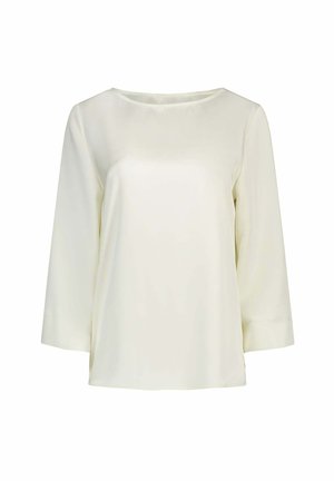 Blouse à manches longues couleur crème avec un col rond et un tissu lisse et léger, présentée sur fond blanc.