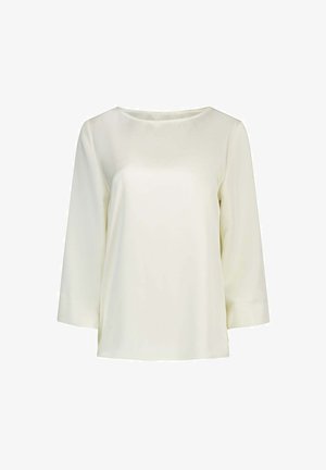 Blouse à manches longues couleur crème avec un col rond et un tissu lisse et léger, présentée sur fond blanc.