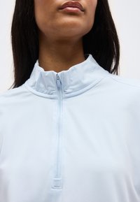 Κοντινό πλάνο ατόμου που φοράει ανοιχτό μπλε τοπ με φερμουάρ κλεισμένο μέχρι τον γιακά, δείχνοντας το λαιμό και το κάτω μέρος του προσώπου.