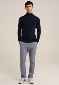 Jūras spēku krāsas turtlenecks ar gaiši pelēkām rakstainām biksēm un pelēkiem sporta apaviem. Tērps ir ar pieguļošu piegriezumu un garām piedurknēm.