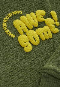 Grüner Strickstoff mit fett gedrucktem, gelbem Teddybuchstaben, auf dem "AWESOME!" steht, und kleinerem Text, der sich darüber krümmt und "MADE FOR YOU BY NPPS" sagt.