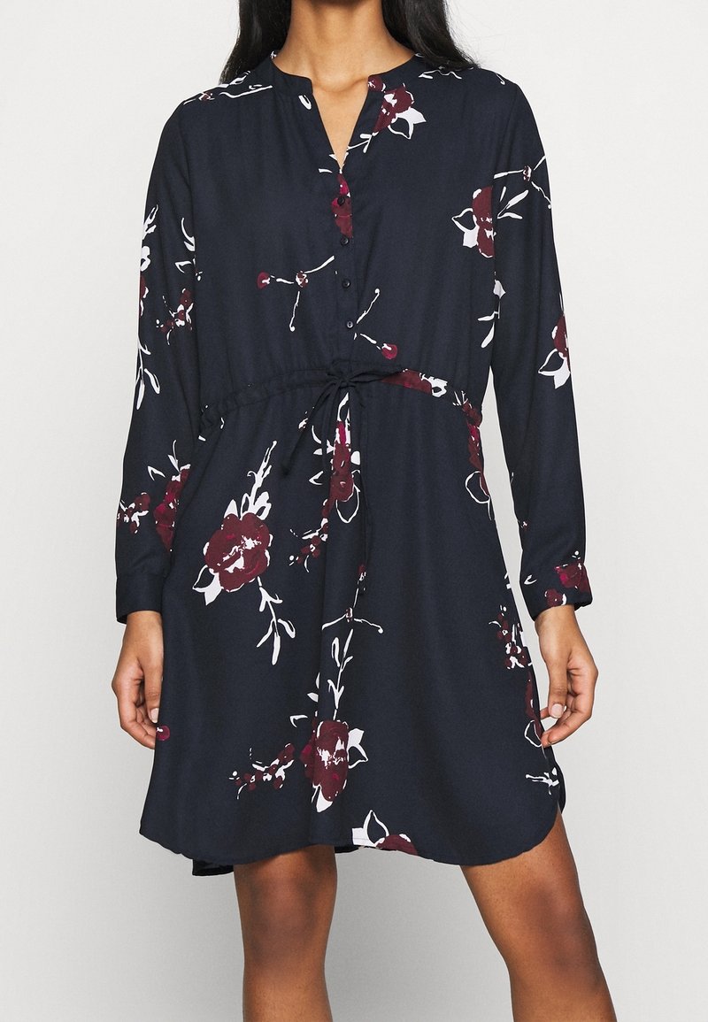 Dunkelblaues Kleid mit langen Ärmeln, Knöpfen vorne, Blumenmuster in Burgunderrot und Weiß sowie einem eingeschnürten Bund für eine verstellbare Passform.