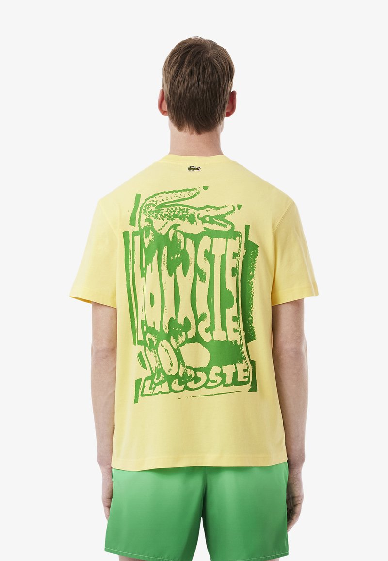 T-shirt en coton jaune avec un grand graphique de crocodile vert et du texte au dos ; manches courtes et col rond.