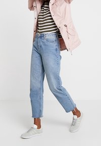 Jeans de mezclilla azul claro con un corte relajado, con dobladillos deshilachados, combinados con una camiseta a rayas y una chaqueta rosa, complementados con zapatillas grises.