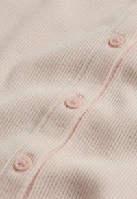 Tissu côtelé rose clair avec des boutons roses assortis cousus en une rangée verticale au centre.