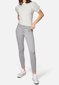 Jeans skinny grigi con orlo leggermente rovinato, abbinati a un top grigio chiaro con maniche a sbuffo e sneakers bianche.