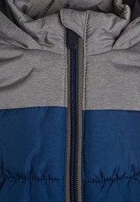 Szara i niebieska kurtka puchowa z zamkiem błyskawicznym, charakteryzująca się gładką fakturą i połączeniem materiałów w designie z blokami kolorów.