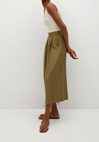 Midi spódnica w oliwkowym kolorze z plisami i wysokim stanem, zestawiona z dopasowanym kremowym topem z prążkowanego materiału i sandałami na ramiączkach w kolorze brązowym.