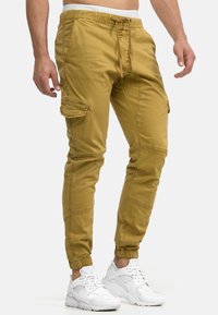 Cargo-Hosen in Khaki, aus Baumwolle, mit einem elastischen Bund, Kordelzugverschluss, seitlichen Taschen und elastischen Bündchen an den Knöcheln.