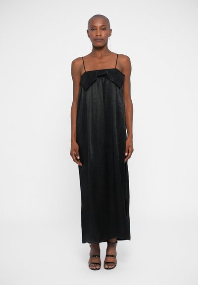 Vestido maxi negro con tirantes finos, que presenta un gran lazo en el pecho. Textura suave, silueta fluida y diseño hasta los tobillos.