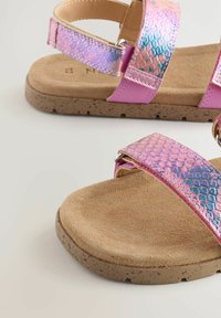 Sandali rosa con cinturini in pelle di serpente iridescenti, suola interna morbida color tan e suola in gomma testurizzata. Inclusi accessori con fibbia regolabile.