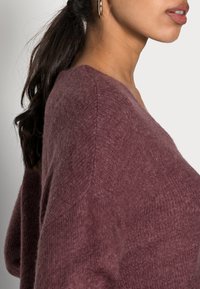 Maglione a maglia bordeaux con scollatura a V e tessuto texture. Caratterizzato da una vestibilità comoda e dettagli a coste sui polsini e sull'orlo.