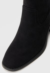 Botine negre din suede, cu vârful ascuțit, detalii cusute și talpă solidă din cauciuc negru. Textură netedă cu un design minimalist.