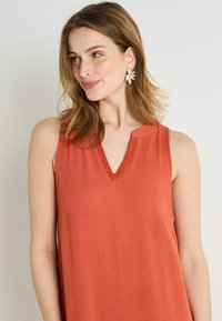 Vestido naranja sin mangas con escote en V y cuello con encaje, que presenta una tela texturizada y un corte relajado. Adecuado para uso casual.