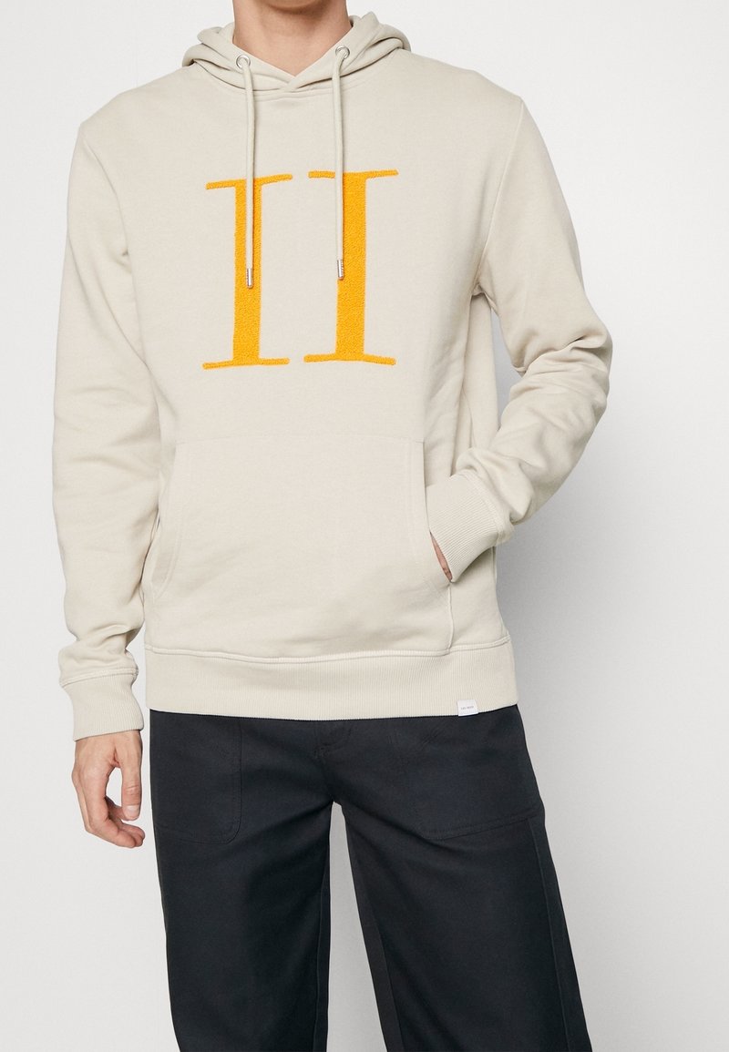 Sudadera crema con un gran gráfico frontal naranja "II". Presenta una capucha con cordón, un bolsillo tipo canguro y puños acanalados.