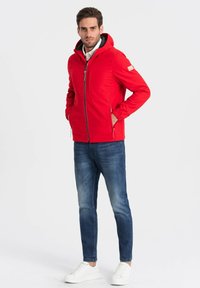 Rød hættetrøje med lynlås, sidelommer og ribbede cuffs. Matched med slim-fit blå jeans og hvide sneakers. Simpelt design.