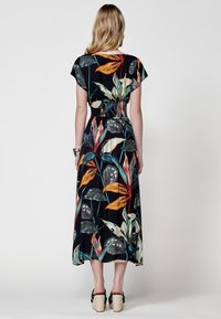 Vestido largo floral con fondo negro y patrones de hojas coloridas en verde, naranja y rojo. Tela fluida con detalle de cintura elástica.