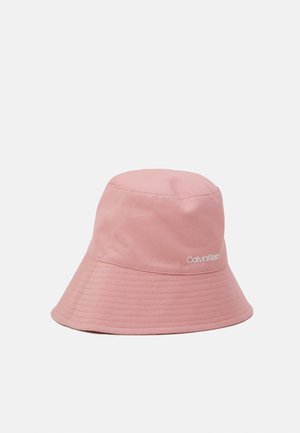 Pink stofbucket hat med bredt syet skyggebind og hvid Calvin Klein-logo på siden mod en ensfarvet lys baggrund.