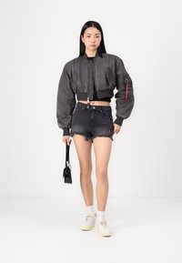 Gray cropped bomber jacket with textured fabric, ribbed cuffs, and a zipper. Paired with black denim shorts and white sneakers.