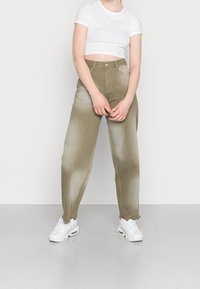 Olijfgroene wijde pantalons met een hoge taille, met een vervaagde textuur; gecombineerd met een witte cropped shirt en witte sneakers.