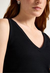 Black ribbed tank top with a deep V-neckline. Close-up view highlighting the fabric texture and shoulder area, paired with circular silver earrings.