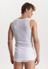 Hvid ribbet tanktop lavet af bomuld, med en ærmeløs design og en tætsiddende pasform. Bæres med matchende hvide trusser.