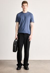 Kék pamut póló kontrasztos gallérral, fekete bőszárú nadrág és fekete táska. A cipők vastag talpúak, lekerekített orrúak és fekete színűek.